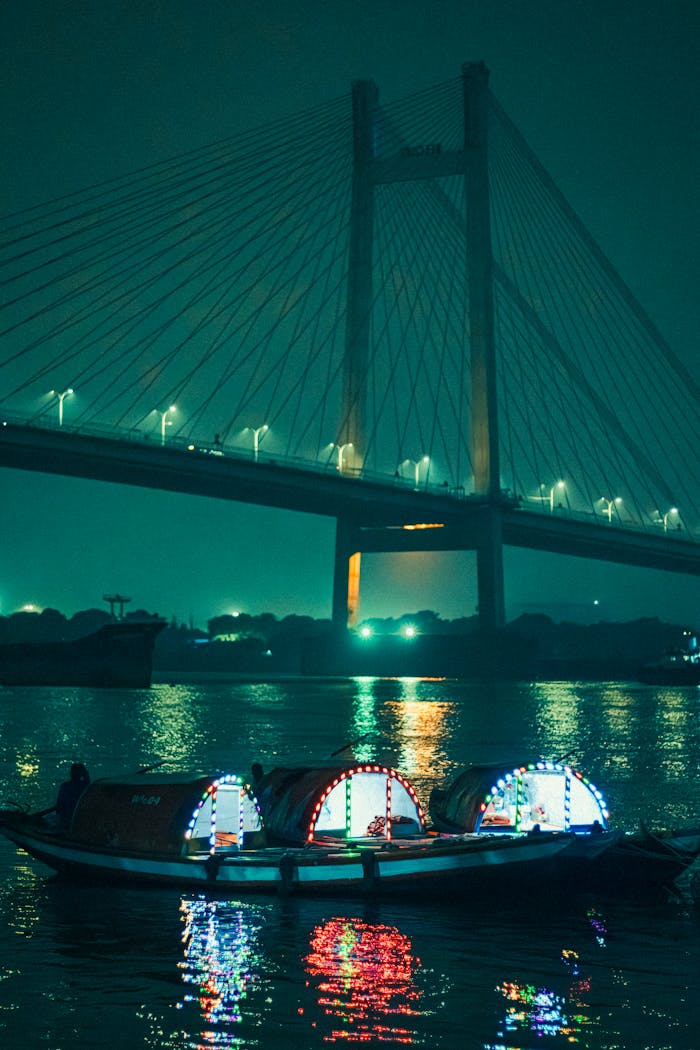 Colorful boats lit under Vidyasagar Setu bridge at night, showcasing Kolkata's vibrant cityscape.