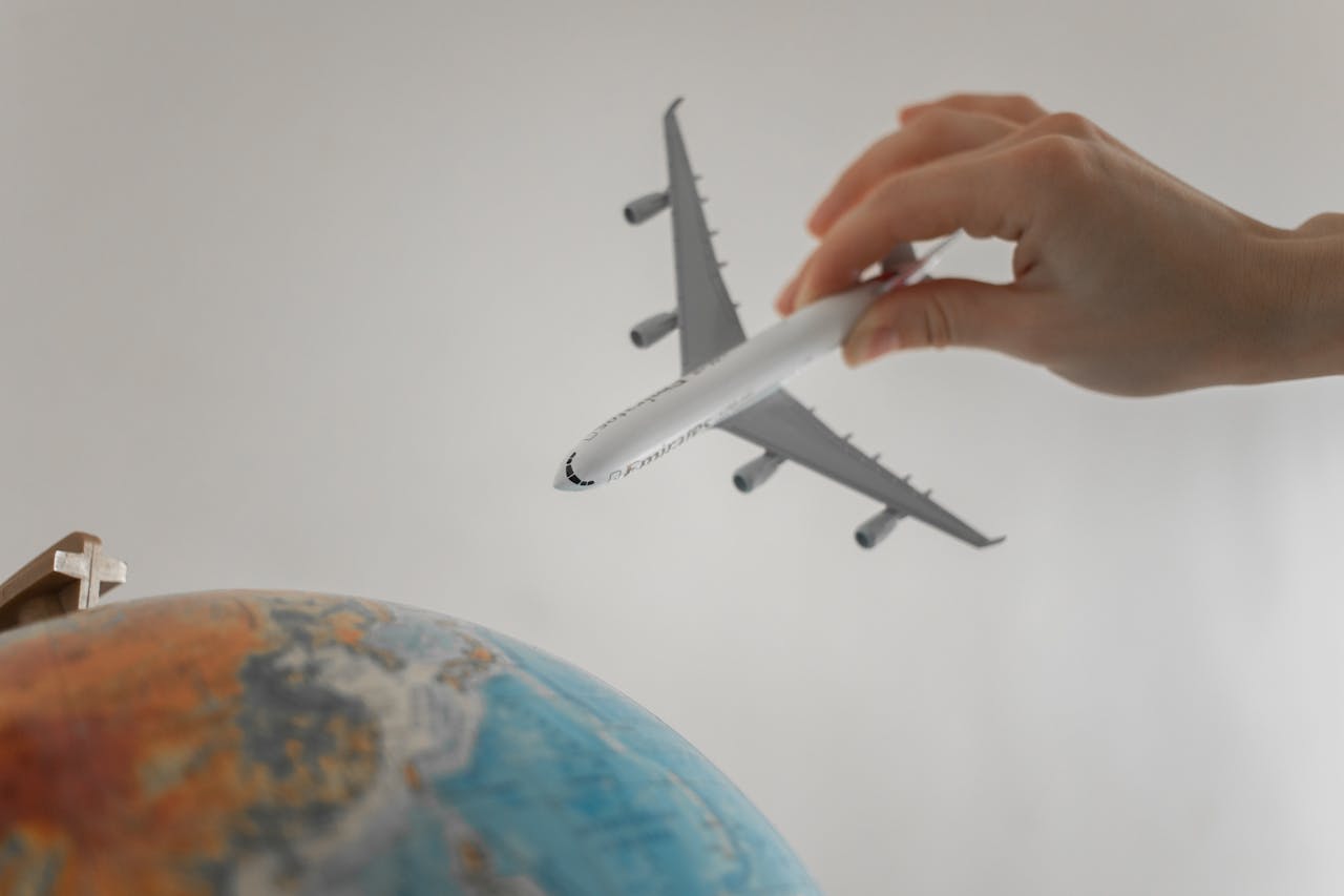 hero-img-01 A hand holds a toy airplane above a globe, symbolizing travel and exploration.